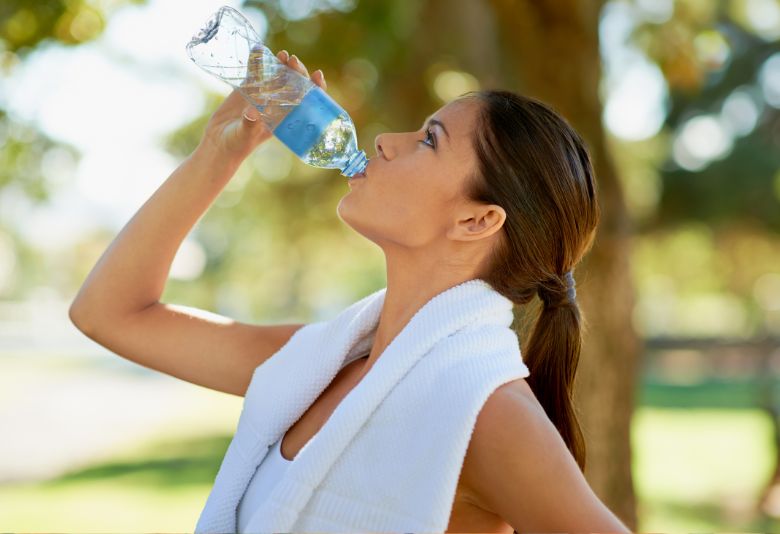 Une femme buvant de l'eau pour rester hydratée pendant le jeûne intermittent, un des éléments essentiels pour profiter de ses bienfaits.